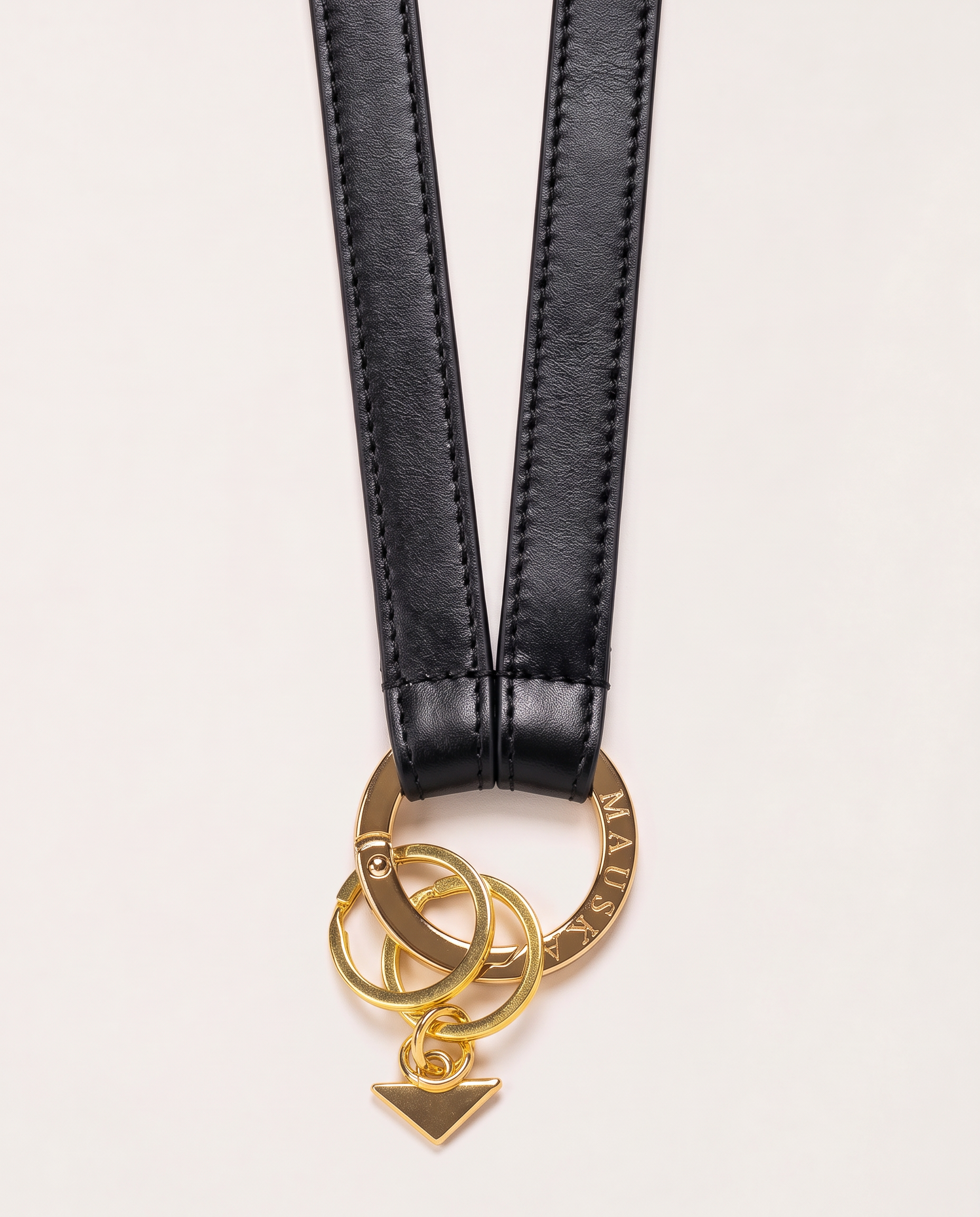 Close-up of MAUSKA ARO black leather key holder with engraved gold-tone circular clasp, key rings and signature triangle charm.