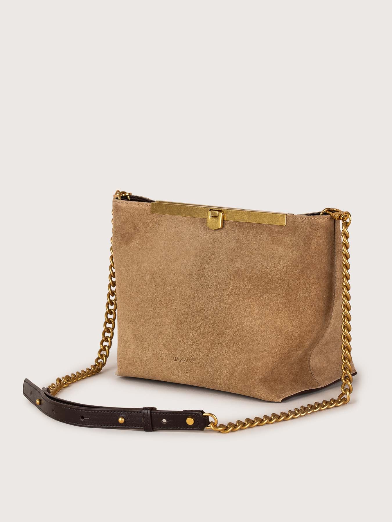 Vista lateral del bolso de piel de ante modelo Petra color arena de la firma Mauska. Accesorio de alta marroquinería diseñado en San Sebastián y fabricado artesanalmente en los talleres de Ubrique, España. Se aprecia la textura premium de la piel de ante y el diseño contemporáneo de autor.