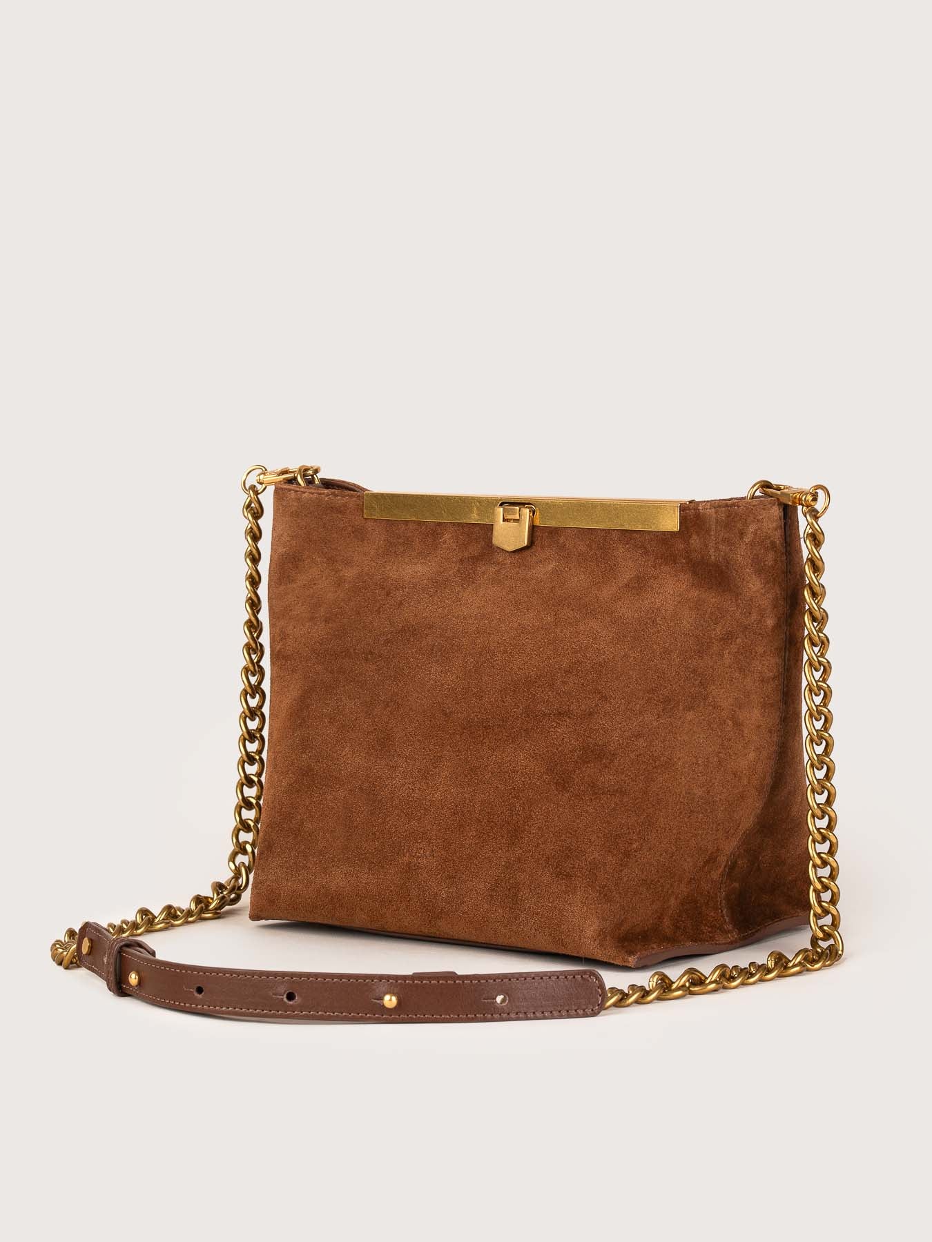 Vista perfil del bolso de piel de ante modelo Petra en color visón de la firma Mauska. Accesorio de alta marroquinería diseñado en San Sebastián y fabricado artesanalmente en los talleres de Ubrique, España. Se aprecia la textura premium de la piel de ante y el diseño contemporáneo de autor.