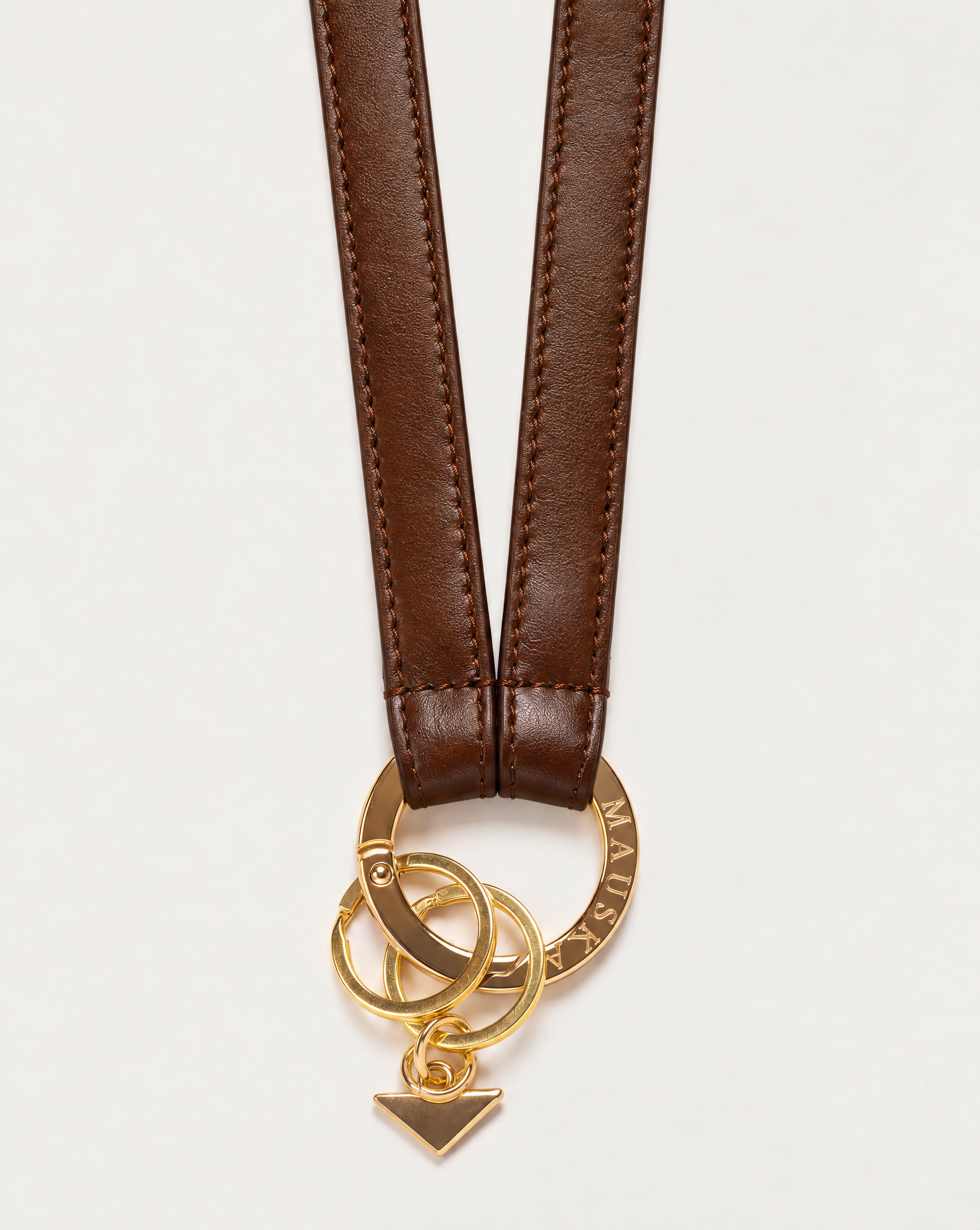 Close-up of MAUSKA ARO tobacco leather key holder with engraved gold-tone circular clasp, key rings and signature triangle charm.