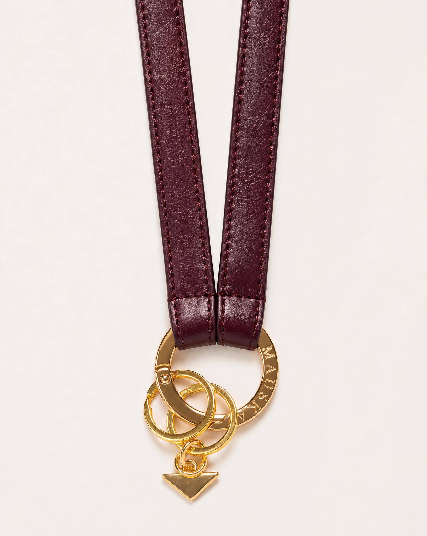 Close-up of MAUSKA ARO burgundy leather key holder with engraved gold-tone circular clasp, key rings and signature triangle charm.