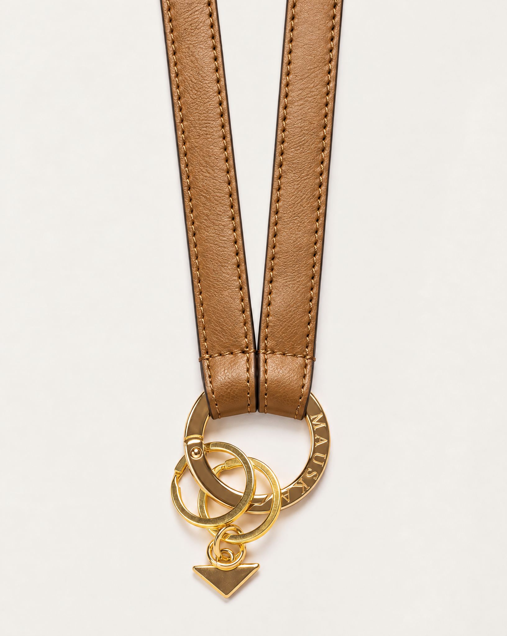 Close-up of MAUSKA ARO natural leather key holder with engraved gold-tone circular clasp, key rings and signature triangle charm.