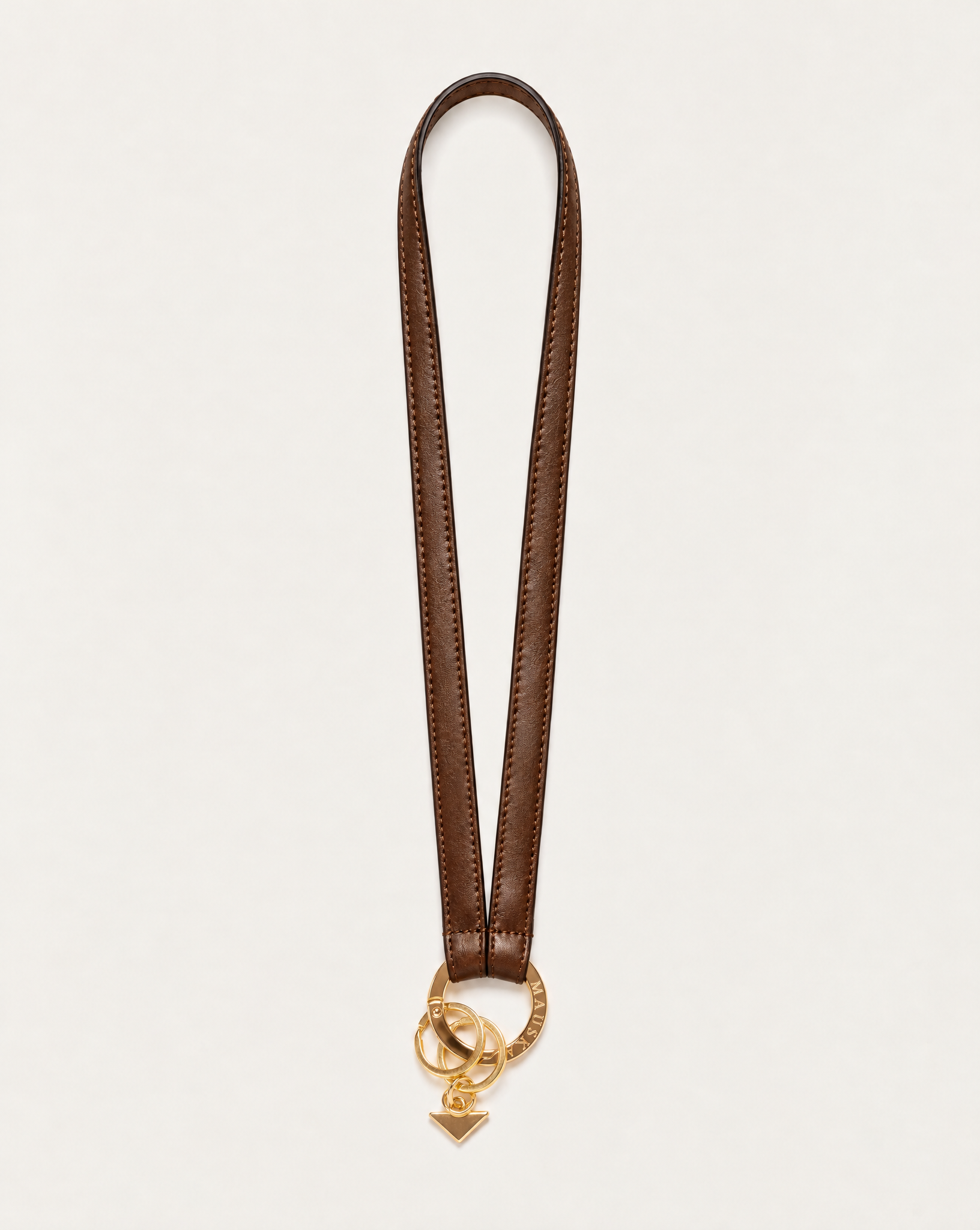 Texto alternativo: Full view of MAUSKA ARO tobacco vegetable-tanned leather neck key holder with gold-tone circular clasp and key rings.